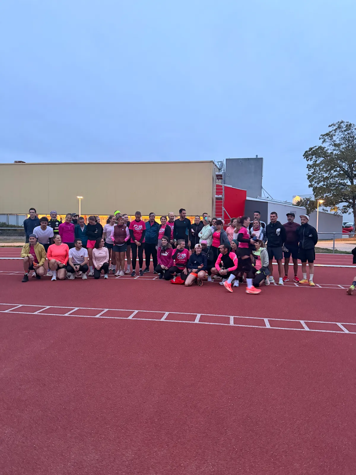 Photo de groupe du Test VMA Octobre Rose au crépuscule sur la piste d'athlétisme, de nombreux participants en tenue rose.