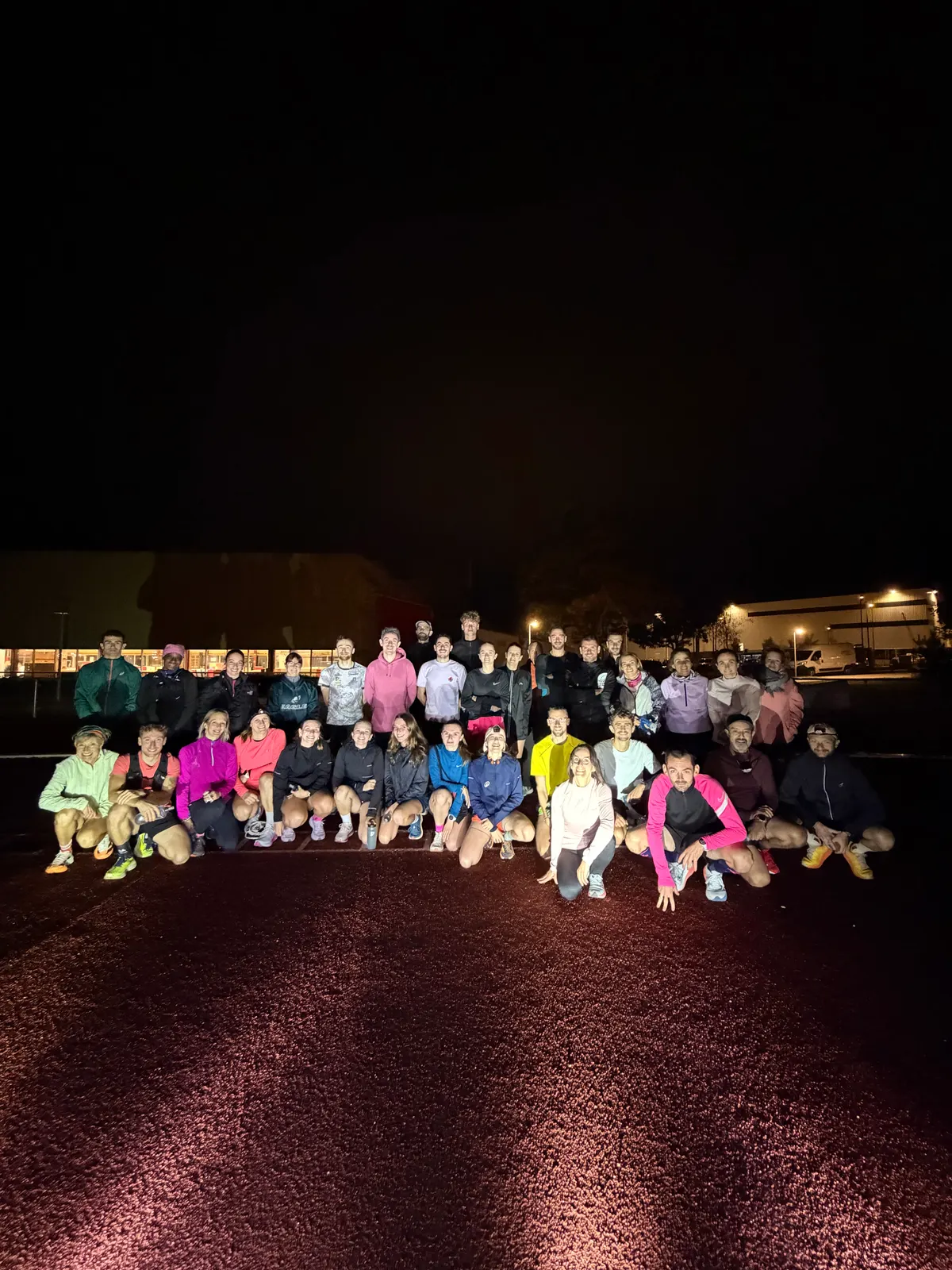Les coureurs du Test VMA Octobre Rose réunis pour une photo de nuit sur la piste d'athlétisme.